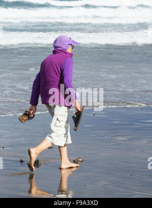 Vieille femme marchant pieds nus sur la plage Banque D'Images