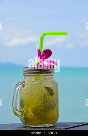 Gros bols style mug plein verre de mojito frais congelé avec capuchon métallique couvercle, paille et orchidée pourpre fleur en café sur la plage Banque D'Images