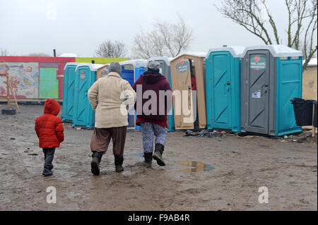 Voir des femmes et des enfants réfugiés dans le camp de réfugiés de la Jungle à Calais comme ils marchent sur l'eau boueuse route vers les toilettes portatives temporaires dans le domaine familial du camp. Banque D'Images