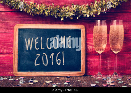 Un tableau sur le texte écrit en 2016 bienvenue, des confettis et une paire de lunettes avec champagne à l'une rustique en bois rouge Banque D'Images