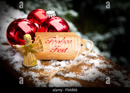 Tag en bois avec les mots 'Frohes Fest" (Joyeux Noël) à côté des boules de noël et l'ange dans la neige Banque D'Images