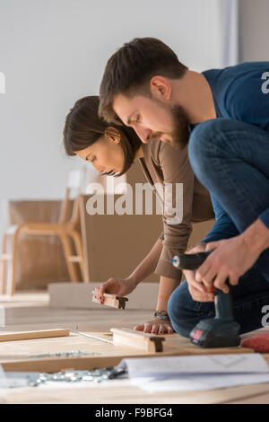 Happy young couple mettre ensemble de meubles à assembler soi-même lorsqu'ils entrent dans leur nouvelle maison. Banque D'Images