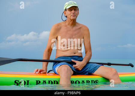 Un 60 ans caucasien homme sourit alors qu'il s'assied sur son bateau pneumatique paddle board dans les Caraïbes, au large de Sainte Croix, Îles Vierges des États-Unis Banque D'Images