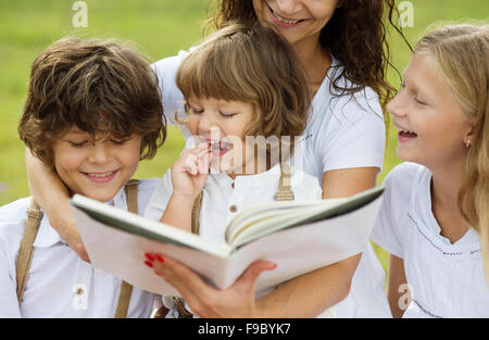 Mère est coin et lire un livre à ses enfants dans le vert du parc Banque D'Images