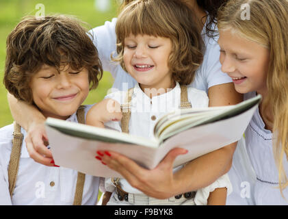 Mère est coin et lire un livre à ses enfants dans le vert du parc Banque D'Images