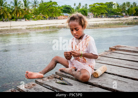 Une petite fille prépare ses outils de pêche tout en étant assis sur la jetée en bois dans l'île tropicale de Arborek à Raja Ampat, Papouasie occidentale. Banque D'Images