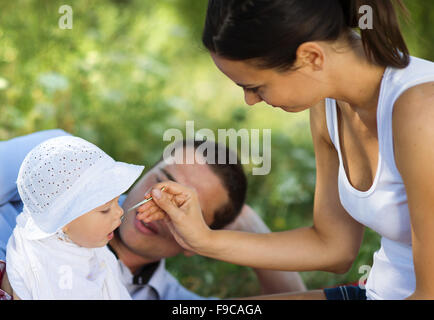 Heureux les jeunes parents de nourrir leur fille à pique-nique. Banque D'Images