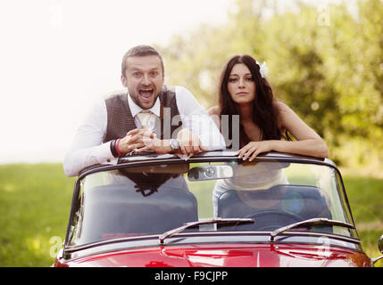 Magnifique mariée et le marié s'amusant avec voiture rétro rouge dans la nature Banque D'Images