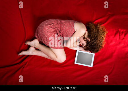 Belle femme triste est couchée sur une couverture rouge avec tablet Banque D'Images