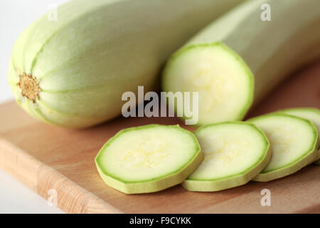 Vert blanc les courgettes en rondelles et l'ensemble à l'aide d'un couteau sur la planche à découper en bois Banque D'Images