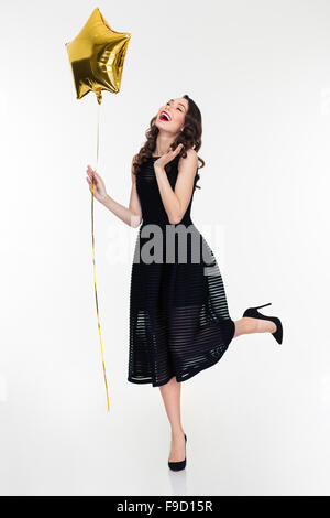 Belle jeune femme frisée style rétro en riant et holding golden star shaped balloon over white background Banque D'Images