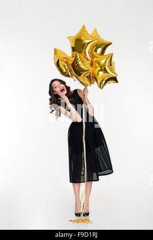 Belle jeune fille gaie amusant bouclés avec retro hairstyle classique en robe noire et des chaussures d'or holding balloons Banque D'Images