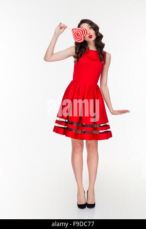 Longueur totale de cute funny drôle curly Girl in red dress avec sucette en forme de coeur sur fond blanc Banque D'Images