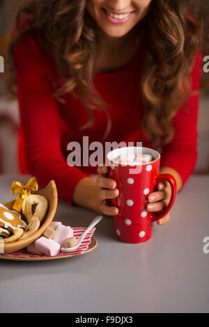 Biscuits de Noël sont une façon merveilleuse de profiter de l'esprit de la saison. Gros plan sur souriante jeune femme avec une tasse de chocolat chaud Banque D'Images