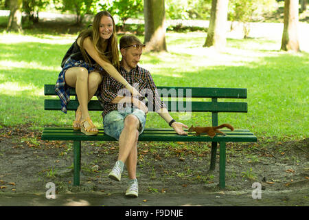 Un jeune couple part-nourrir un écureuil sur un banc de parc. Banque D'Images