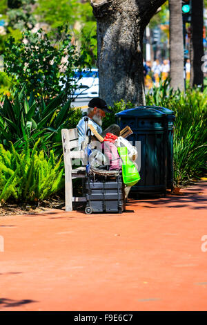 Homme sans foyer avec tous ses effets personnels est assis sur une banquette de la rue au centre-ville de Santa Barbara, CA Banque D'Images