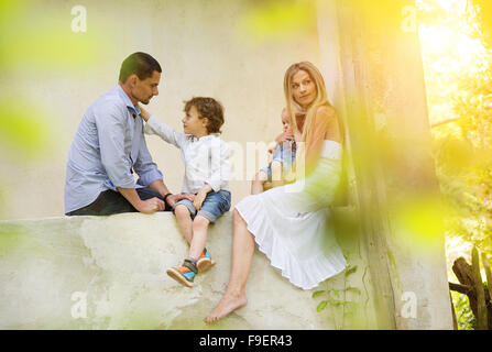 Jeune famille heureuse de passer du temps ensemble assis dehors sur le perron de la vieille maison. Banque D'Images