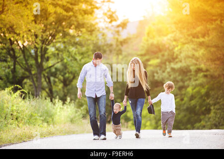 Heureux jeune famille marchant sur la route à l'extérieur dans la nature verte. Banque D'Images