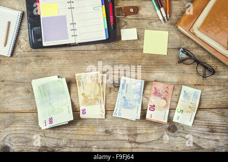 Mélange de fournitures de bureau, gadgets et de l'argent sur une table en bois. Vue de dessus. Banque D'Images