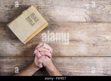 Mains de jeune homme priant Bible et sur un arrière-plan d'un bureau en bois. Banque D'Images