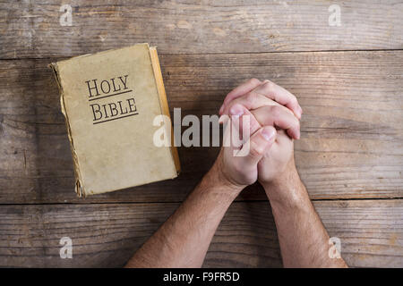 Mains de jeune homme priant Bible et sur un arrière-plan d'un bureau en bois. Banque D'Images