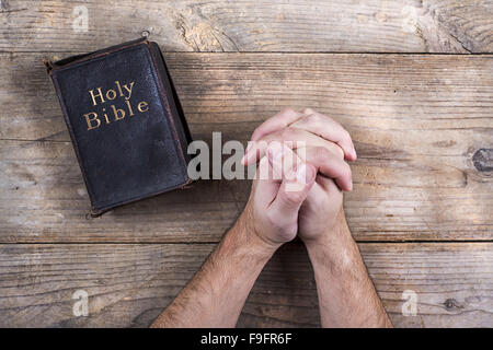 Mains de jeune homme priant Bible et sur un arrière-plan d'un bureau en bois. Banque D'Images