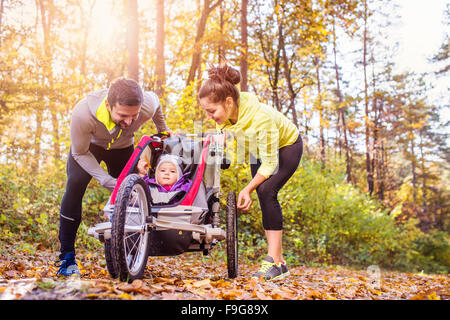 Beau jeune famille avec bébé en poussette fonctionne en dehors de la nature en automne Banque D'Images