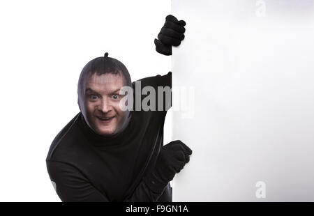 Voleur avec passe-montagne sur son visage, vêtus de noir, tenant une bannière vide. Studio shot sur fond blanc. Banque D'Images