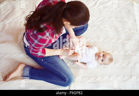 Cute little baby girl s'habiller par sa mère sur un tapis dans un salon. Banque D'Images