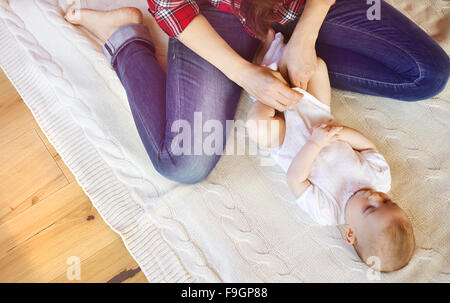 Cute little baby girl s'habiller par sa mère sur un tapis dans un salon. Banque D'Images