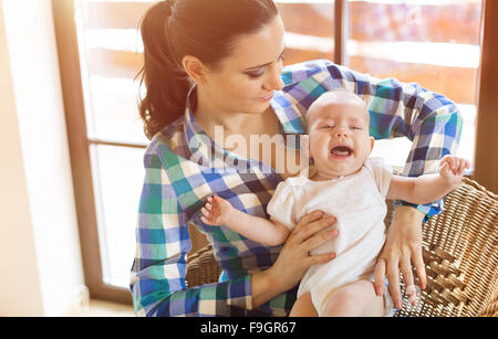 Petit bébé pleurer dans les bras de sa mère dans un salon. Banque D'Images