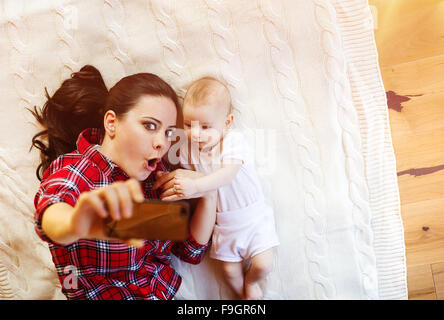 Cute little baby girl et sa mère en tenant sur une couverture selfies dans un salon. Banque D'Images