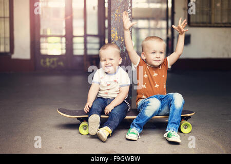 Mignon petit garçons assis sur une planche à roulettes sur leur marche dans la ville Banque D'Images