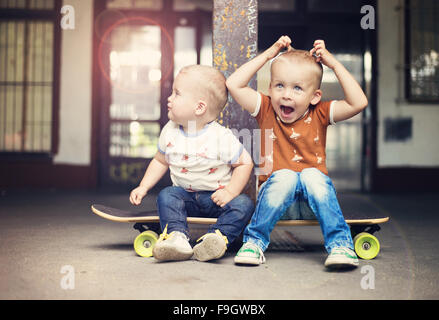 Mignon petit garçons assis sur une planche à roulettes sur leur marche dans la ville Banque D'Images