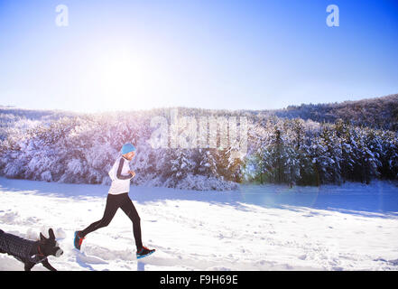 Jeune sportif jogging avec chien à l'extérieur dans le parc d'hiver ensoleillé Banque D'Images