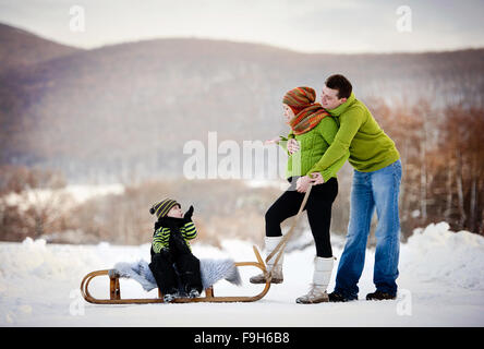 Les parents heureux avec leur fils à cheval sur un traîneau s'amusant à l'extérieur dans la neige. Banque D'Images