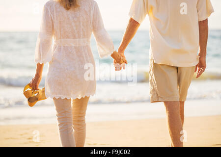 Happy Romantic Couple d'âge moyen bénéficiant beau coucher du soleil à pied sur la plage Holding Hands Banque D'Images