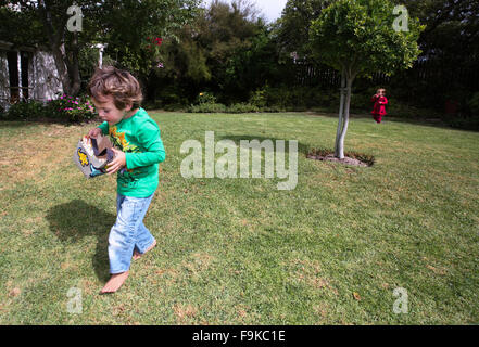 Les jeunes enfants recueillir les oeufs de pâques sur une chasse de Pâques dans un jardin. Banque D'Images