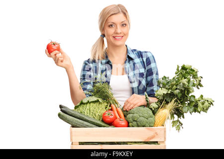 La productrice debout derrière une caisse pleine de légumes frais et tenant une tomate unique isolé sur fond blanc Banque D'Images