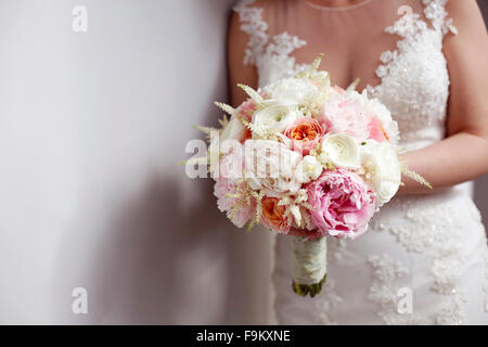 Bride holding bouquet coloré à côté de mur blanc Banque D'Images
