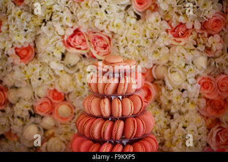 Macaron délicieux sur le stand à côté de mur plein de roses Banque D'Images