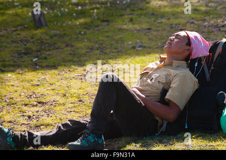 Jeune homme avec bandana rose pose repos sur son sac à dos dans le soleil dort Banque D'Images