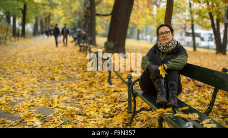 Une femme assise sur un banc dans le parc de l'automne. Banque D'Images