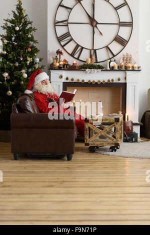 Santa Claus boire du lait et de la lecture livre près de cheminée à la maison Banque D'Images