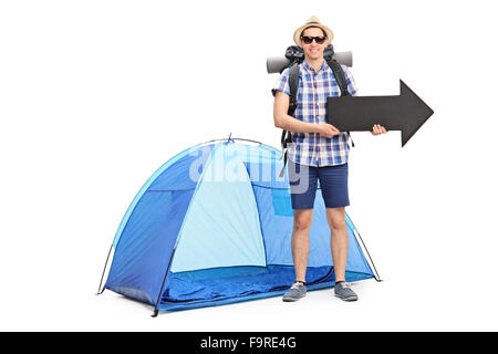 Les jeunes camping-debout devant une tente bleue et tenant une grande flèche noire pointant vers la droite isolé sur fond blanc Banque D'Images