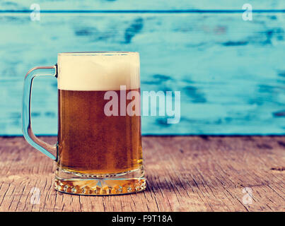Bière servi dans une tasse en verre sur une surface en bois rustique, contre un fond bleu en bois rustique Banque D'Images