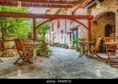 Restaurant italien pays de plein air,chaises en bois et des tables avec l'argenterie, des serviettes et des tasses dans un patio d'arches en maçonnerie. Banque D'Images