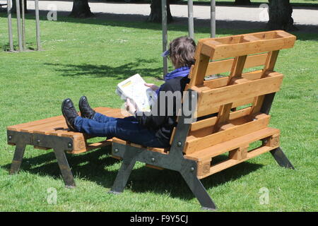 Personne lisant un journal sur une grande chaise en bois dans un parc Banque D'Images