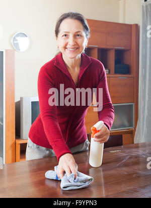 Mature Woman cleaning table avec cleanser et rag a salle de séjour Banque D'Images