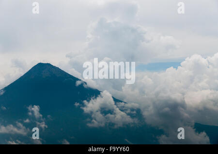 Grand sommet du volcan entouré de brouillard et d'épais nuages sur champ vert Banque D'Images